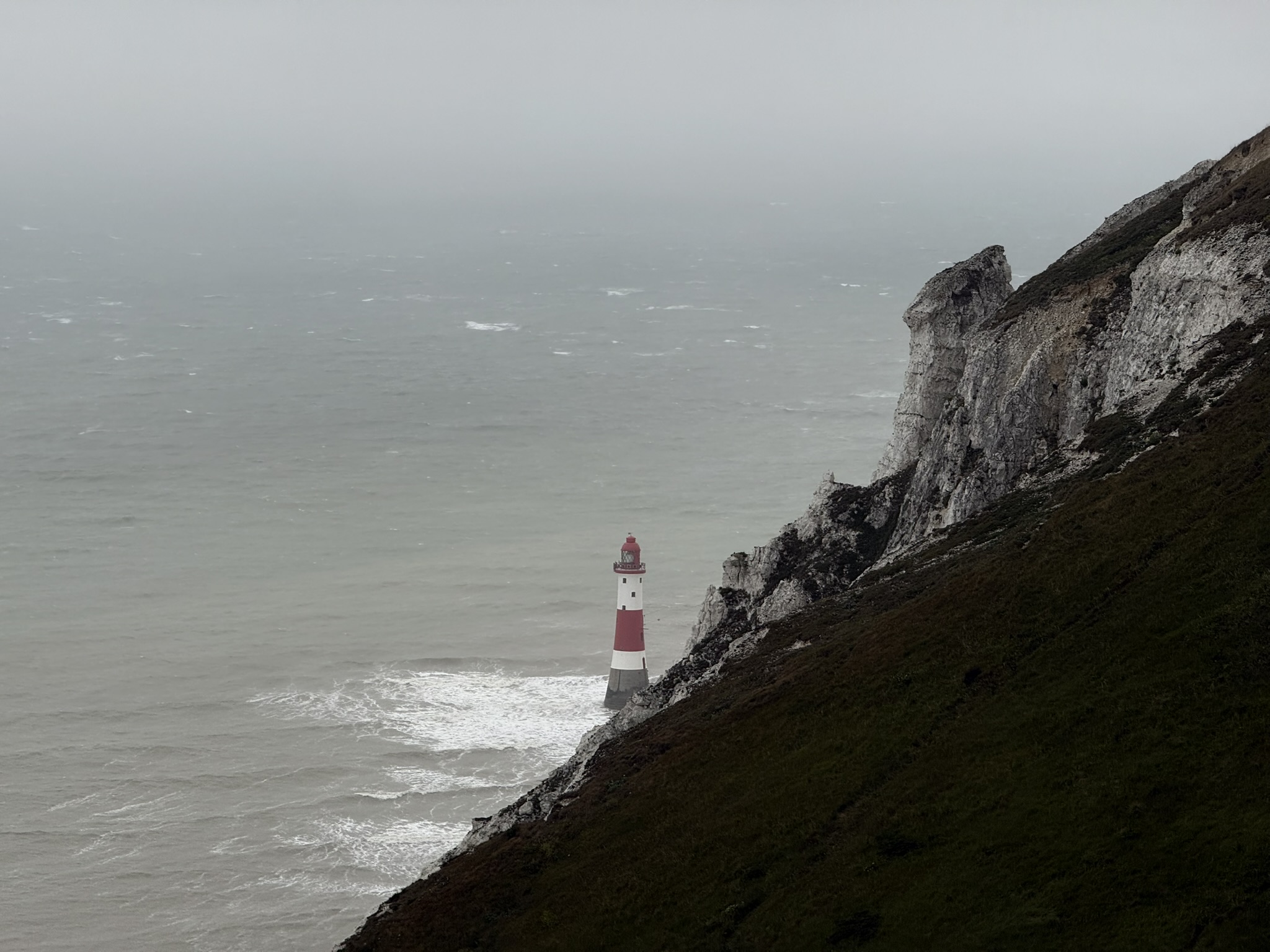 A pale lighthouse embedded in a grey chalk cliff above the sea